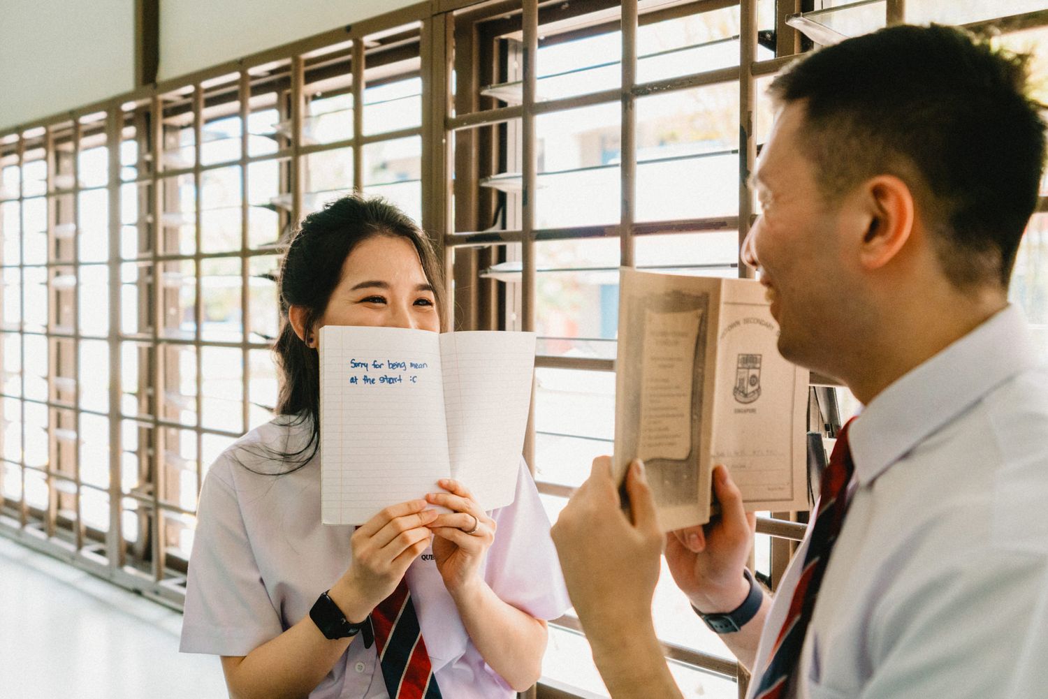 Students engaged in conversation while holding papers in a school classroom setting.