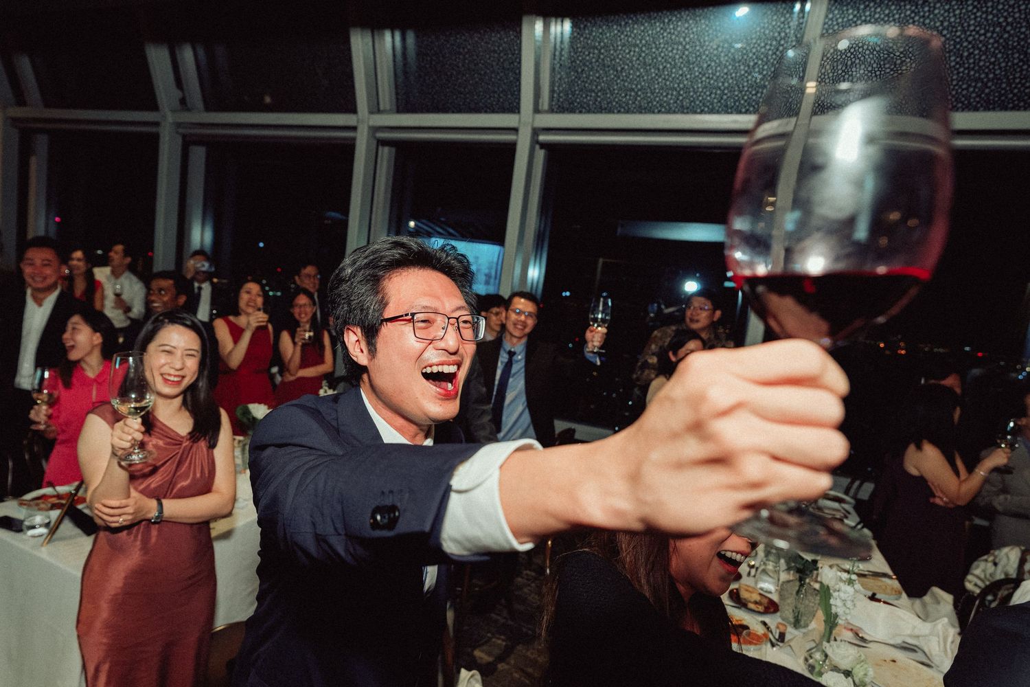 Wedding guest enthusiastically raises a glass during reception celebration.