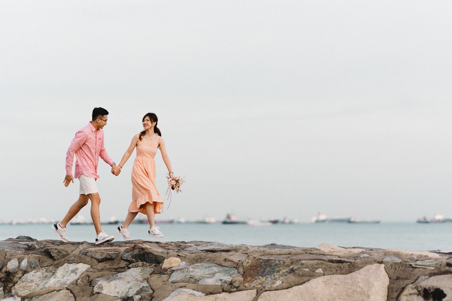 Couple walking and playing along a rocky beach shoreline at sunset.