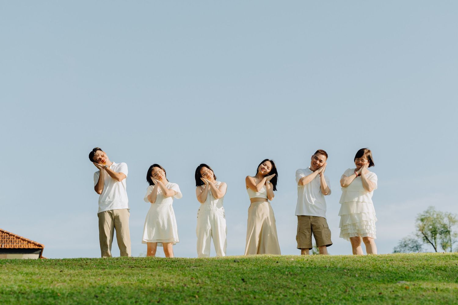 A group of people in neutral colored clothing stand on a grassy hilltop against a blue sky.