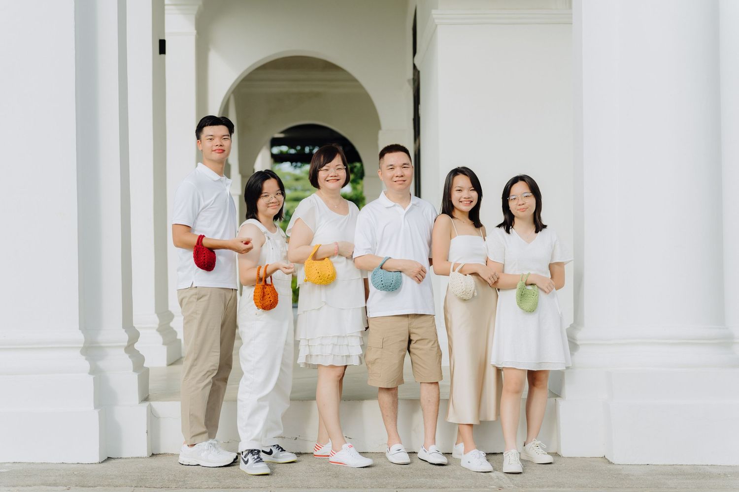 Family wearing coordinated white and beige outfits poses together in an elegant white arched hallway.