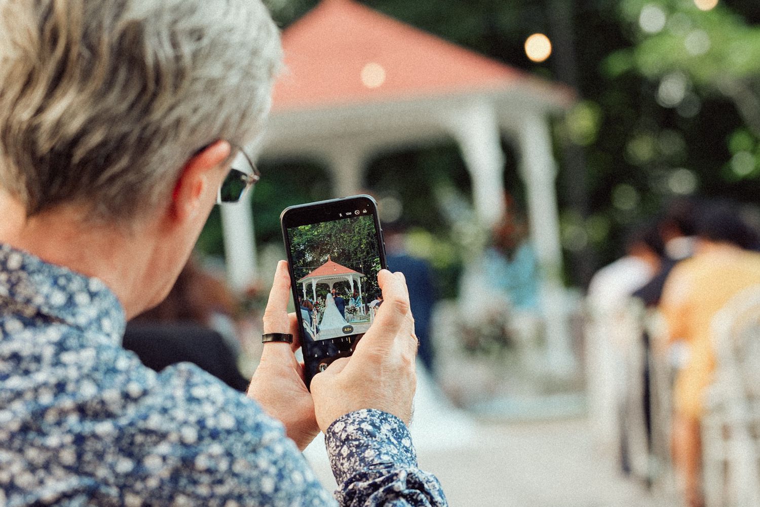 A person using a smartphone to capture photos of trees and nature while walking outdoors.