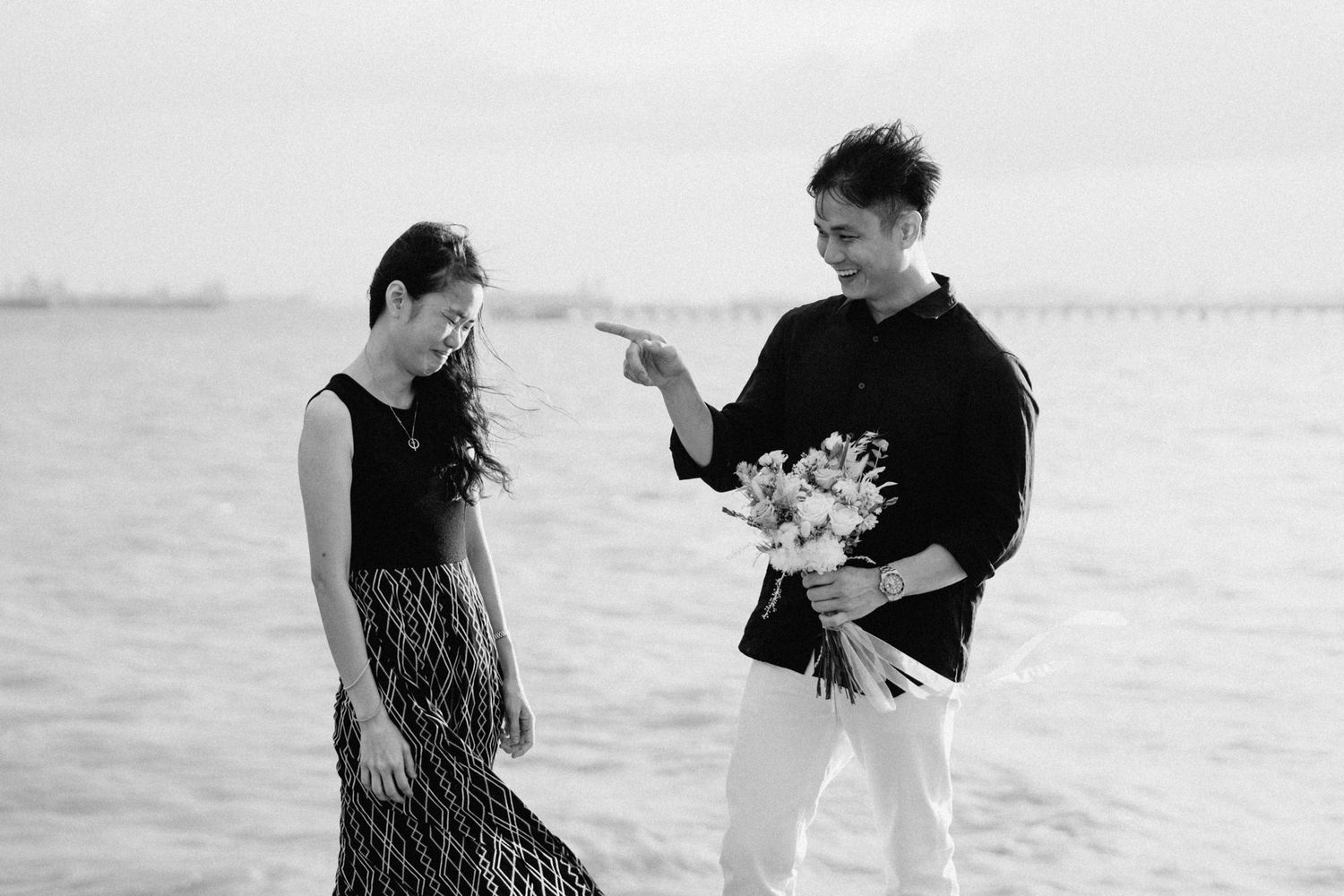Two people share an intimate moment by the ocean with a floral bouquet.
