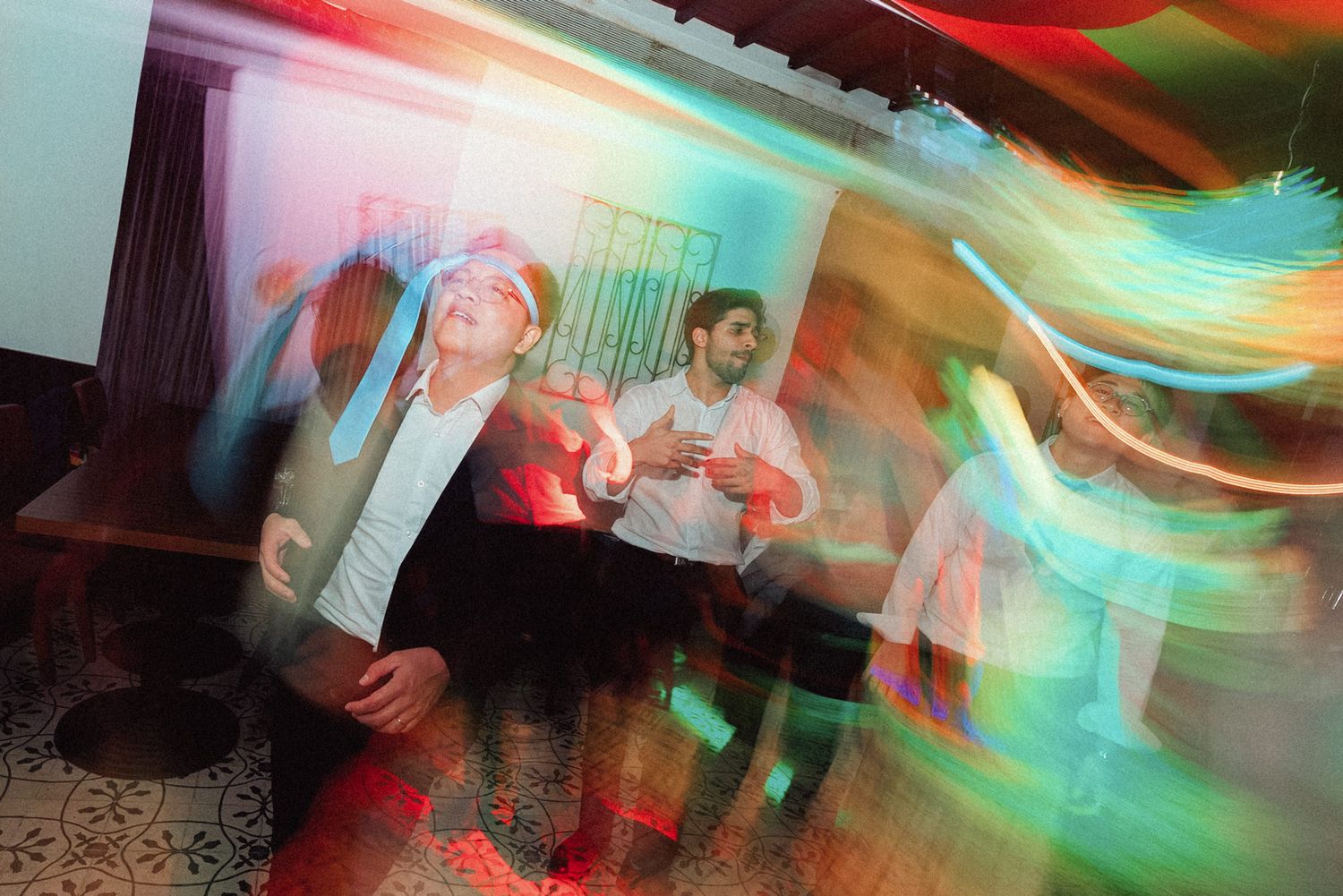 Motion-blurred dance floor scene with colorful red and turquoise lighting effects at a party.