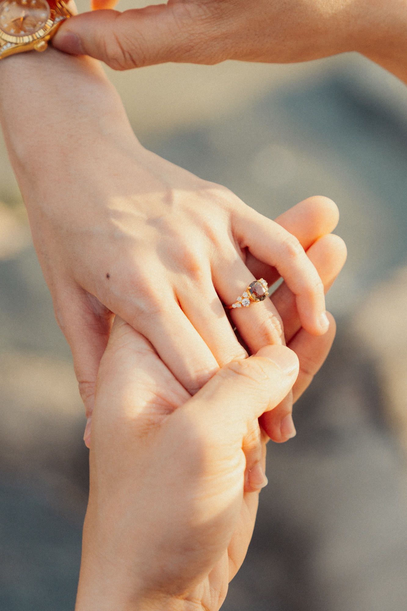 Close-up of hands holding each other tenderly with an engagement ring visible.