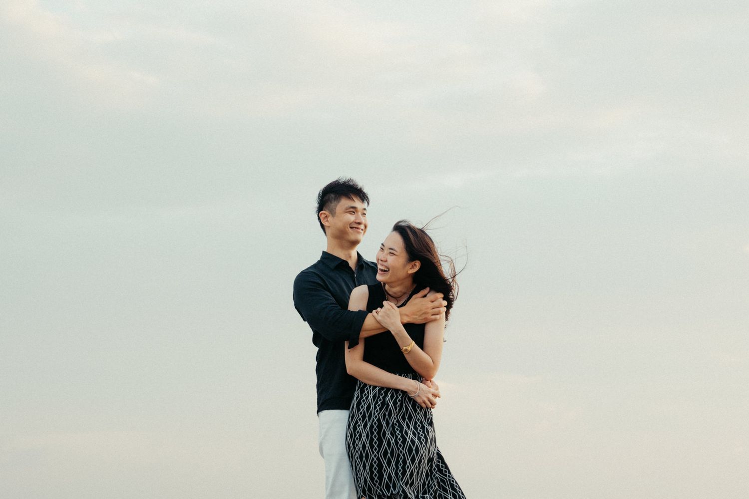Couple embracing and laughing together during a beach photoshoot.