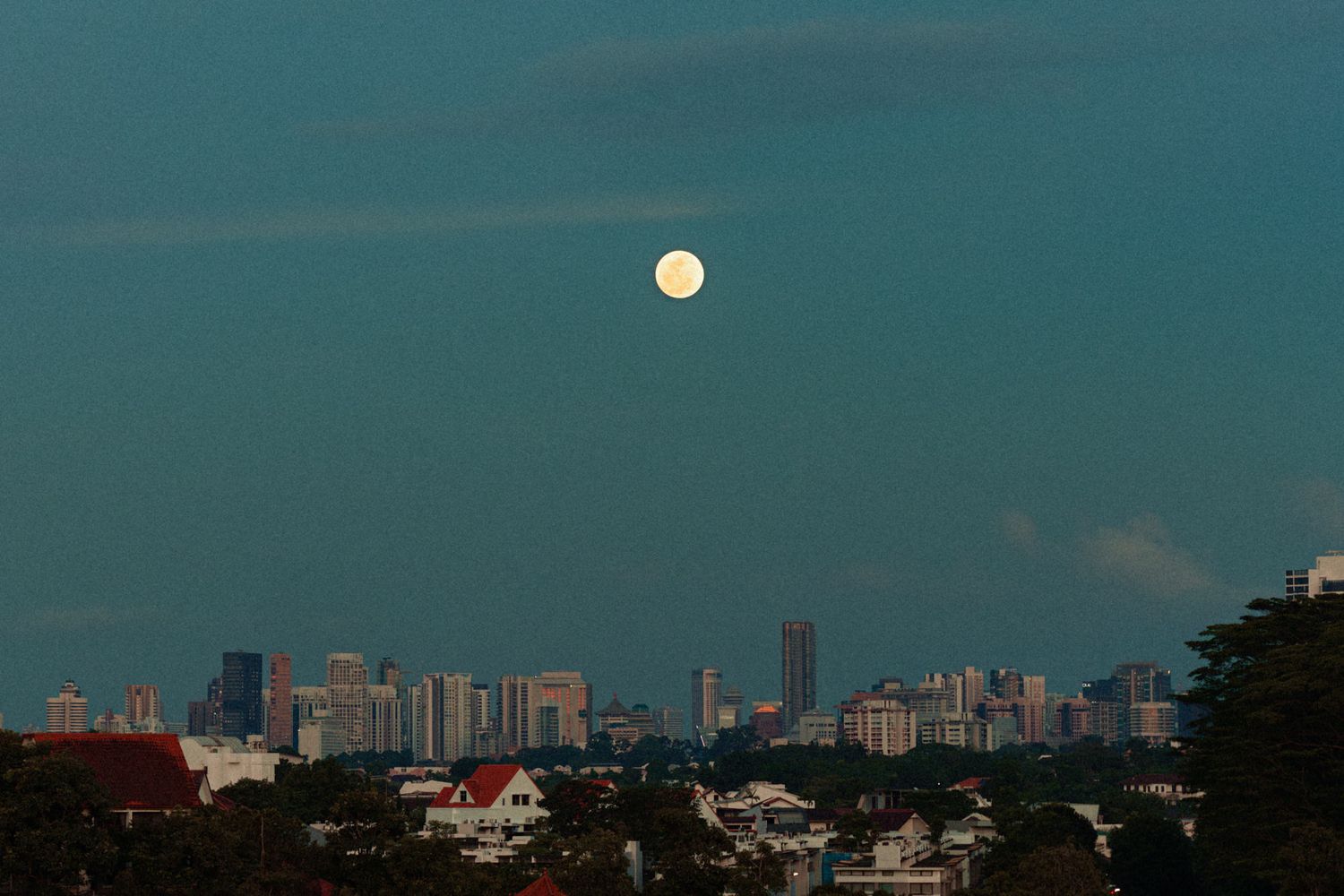 Urban skyline panorama with full moon rising against a teal evening sky.
