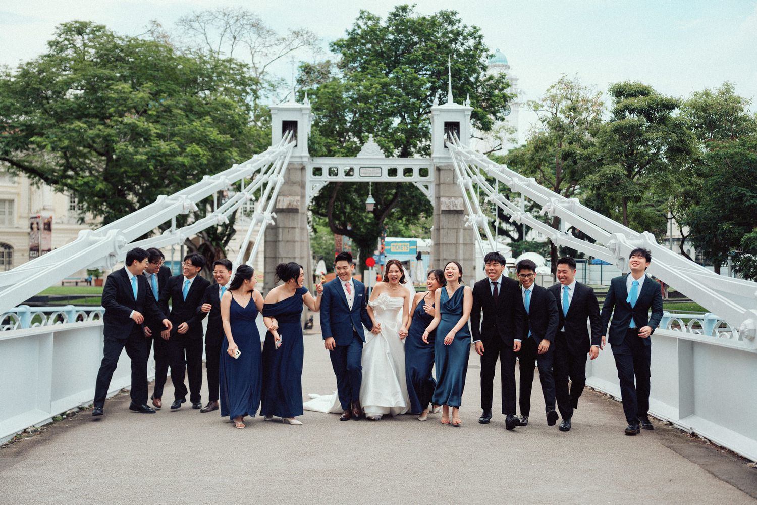 Wedding party poses on a white ornate bridge, bride and groom centered with groomsmen and bridesmaids in navy blue.