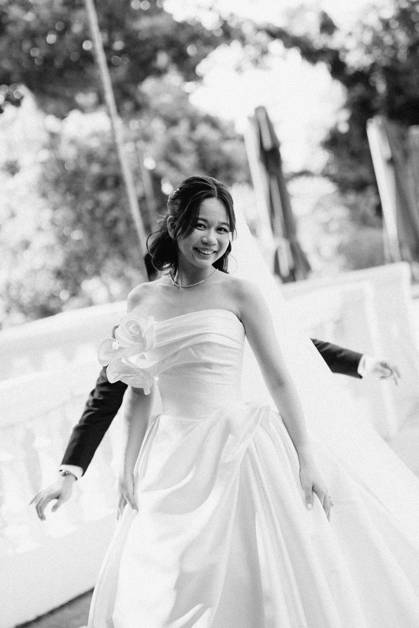A bride in a flowing white wedding dress twirls joyfully outdoors in a series of candid black and white photos.