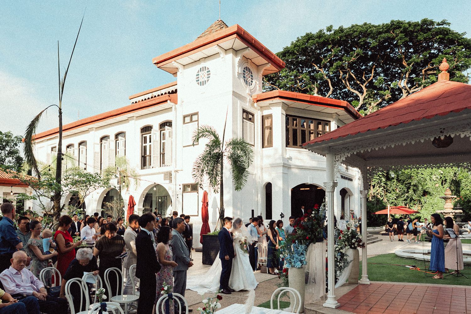 A Spanish colonial style venue with white walls and terracotta roof hosts an outdoor wedding celebration.