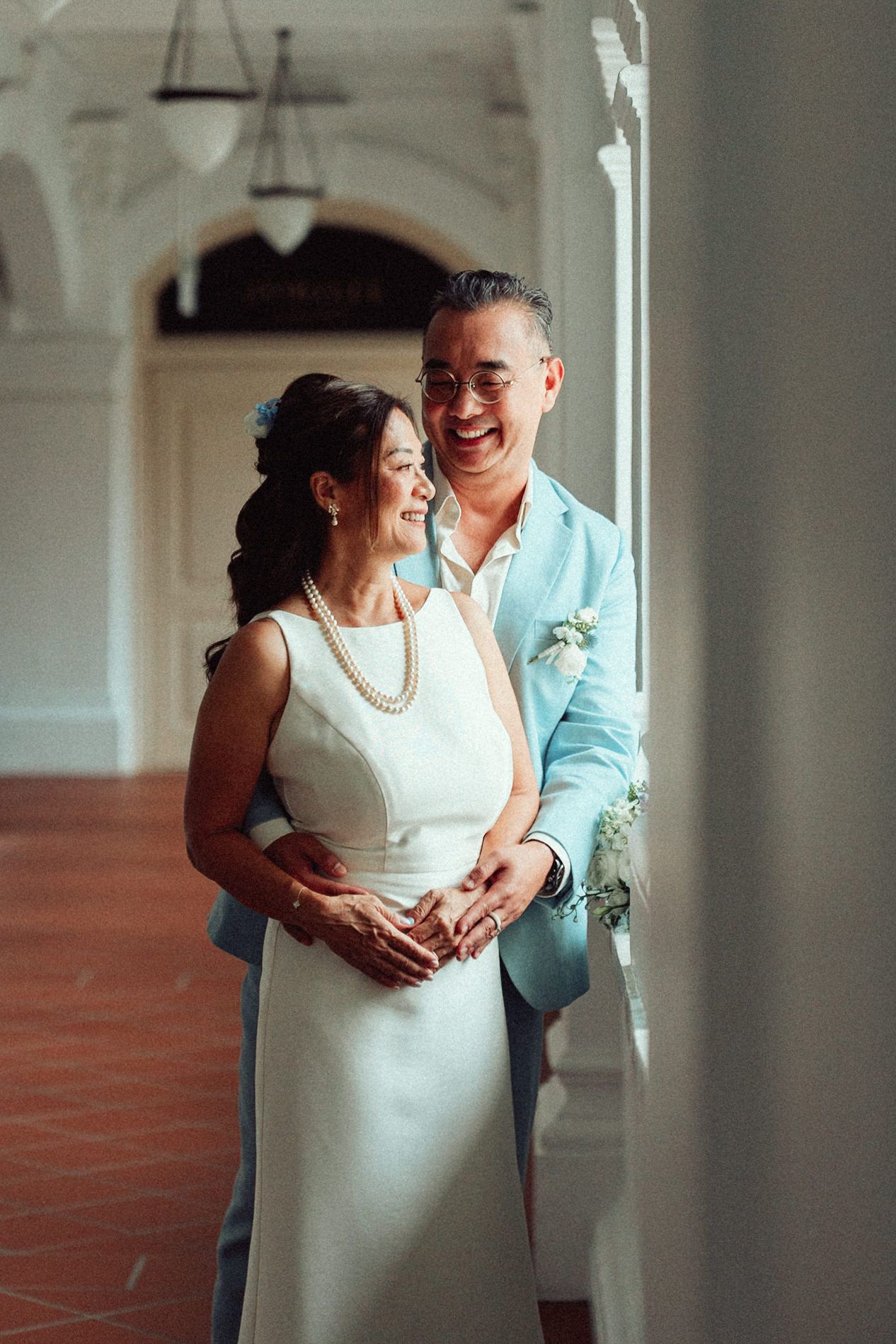 A romantic couple shares an intimate moment in a white dress and blue shirt against a bright interior setting.