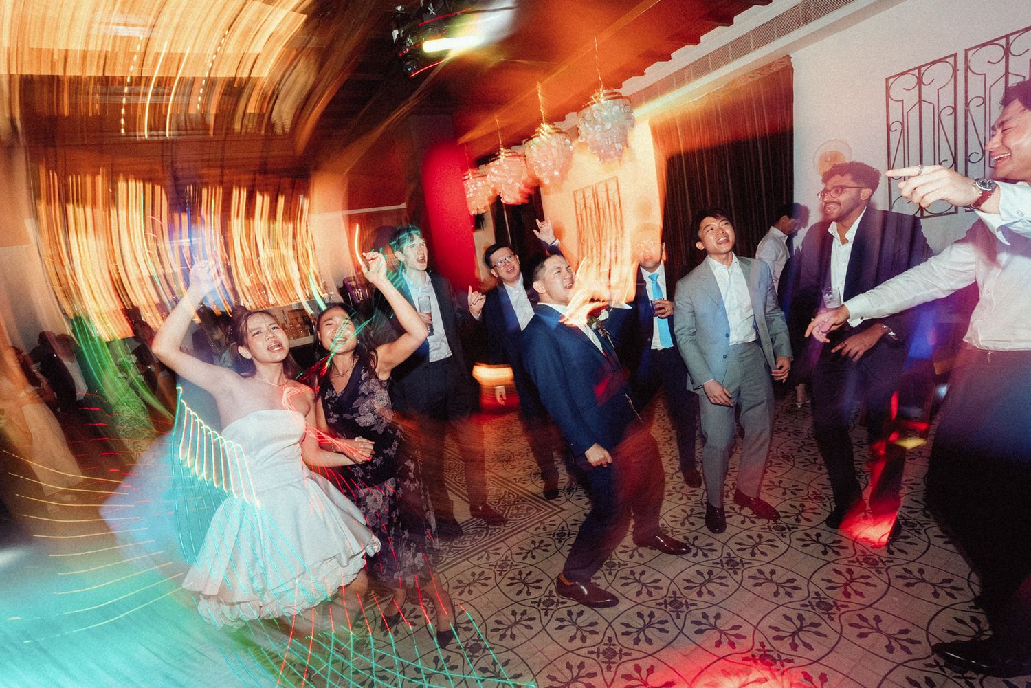 Wedding reception guests dancing energetically on the dance floor with motion blur and colorful lighting effects.