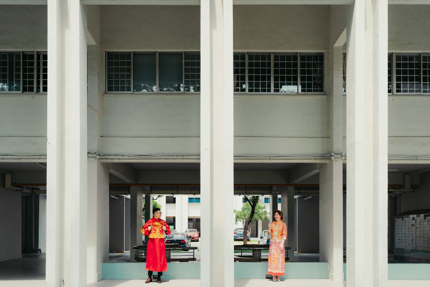 Two people in traditional attire stand beneath concrete columns of a modern building facade.