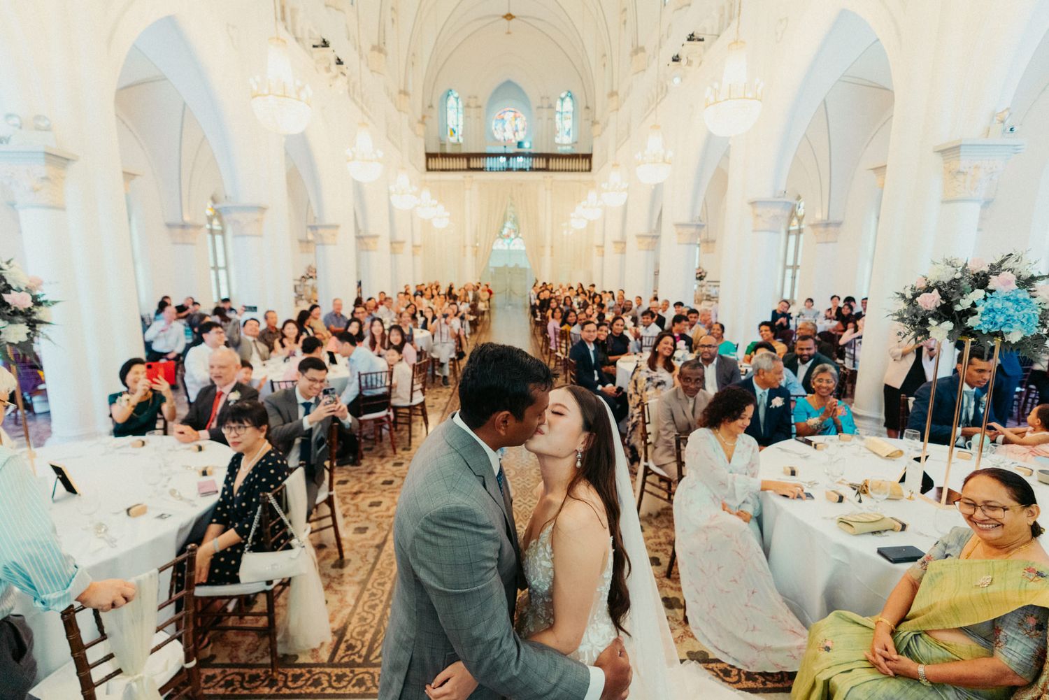 Bride and groom share a kiss at elegant church wedding reception filled with guests seated at decorated tables.