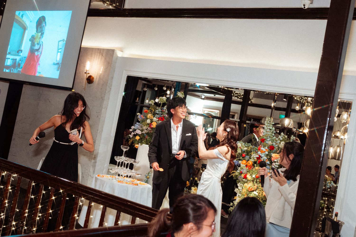 Elegant indoor party with guests celebrating near a decorated Christmas tree and a TV screen displaying a presenter.