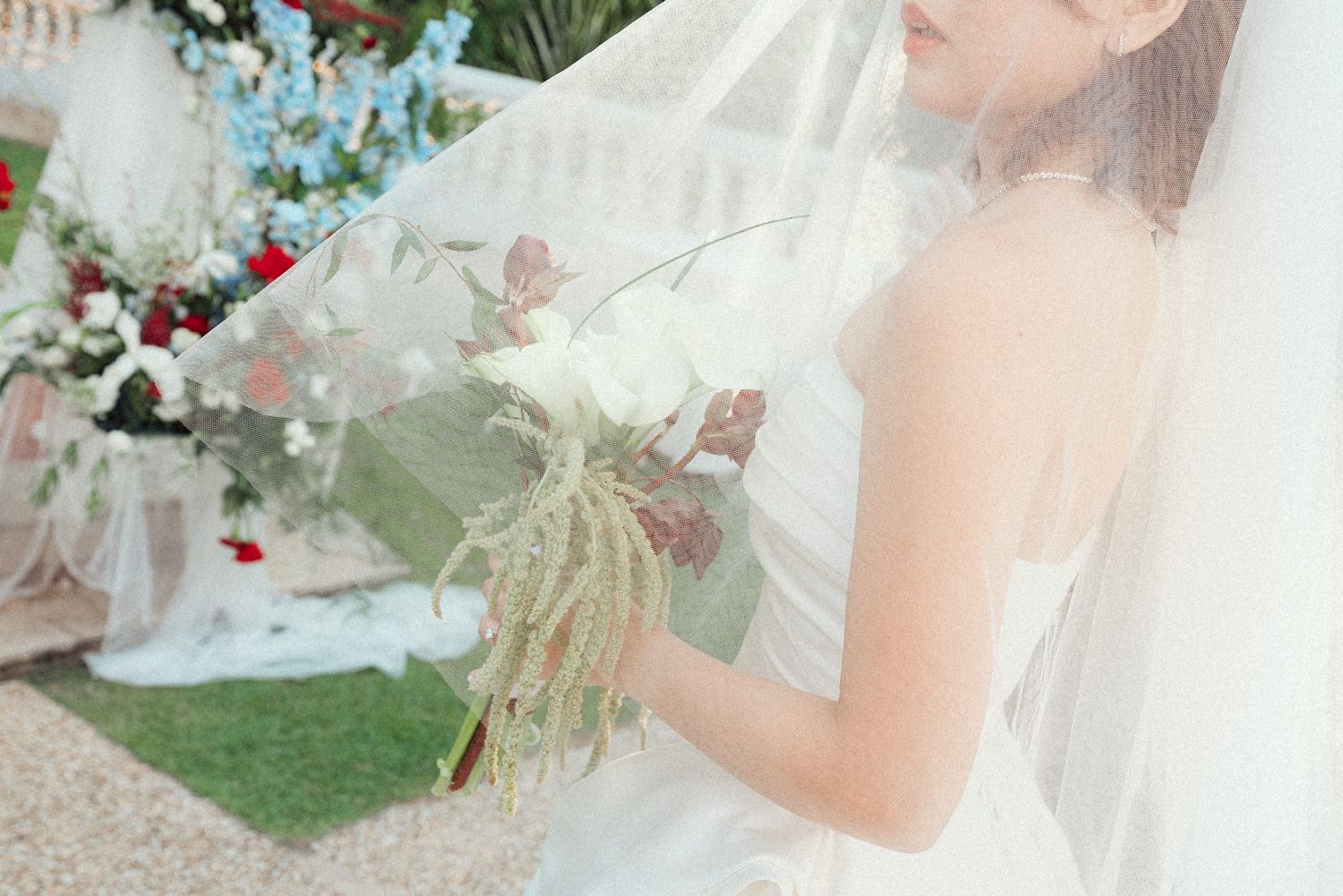 A bride in a flowing white veil and wedding dress poses gracefully in a lush garden setting.