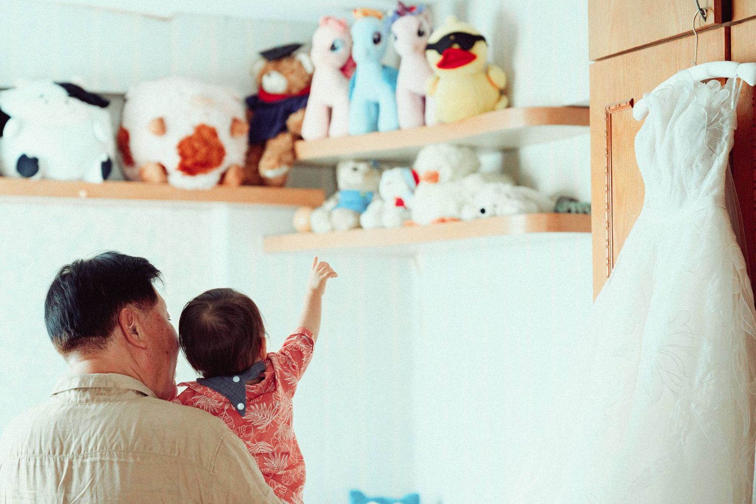 Parent and child looking at stuffed animals displayed on a shelf near a wedding dress.