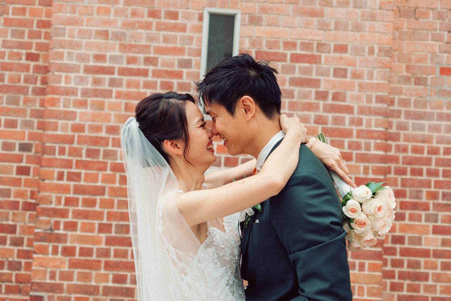 Romantic wedding couple embracing against rustic brick wall.