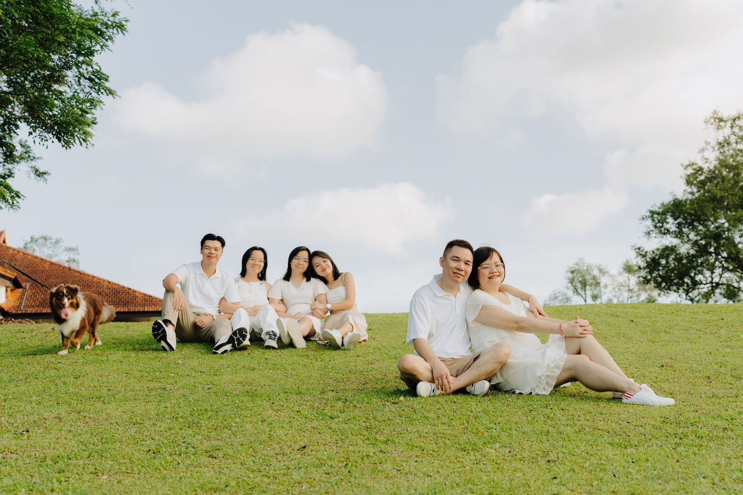 A group in white outfits lounges on a grassy hillside during a sunny outdoor photo session.