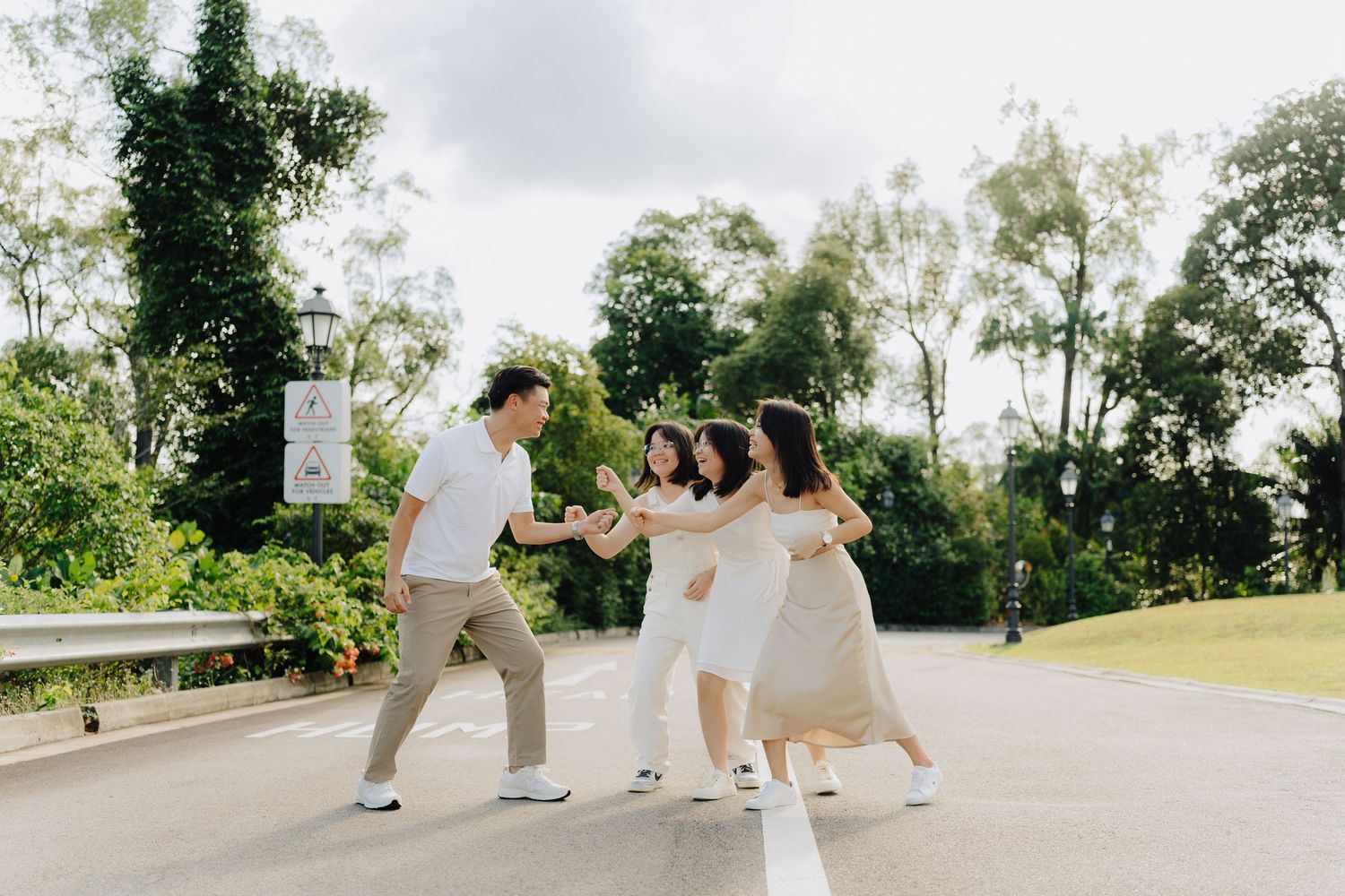 A group of friends walking in a line while holding hands on a paved path during a sunny summer day.