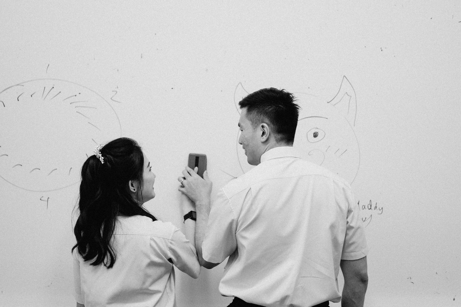Students in white uniforms interacting near a whiteboard in a classroom setting.