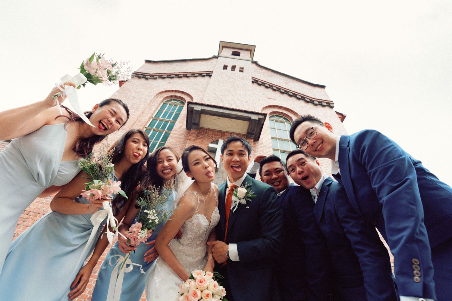Wedding party posing playfully outside brick church building.