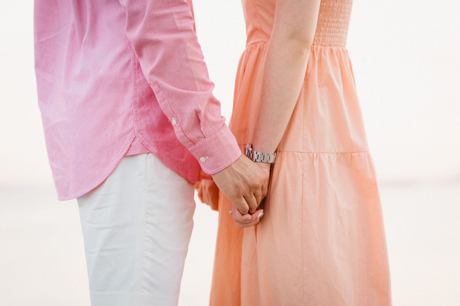 Close-up of couple in pink and peach outfits embracing by the ocean.