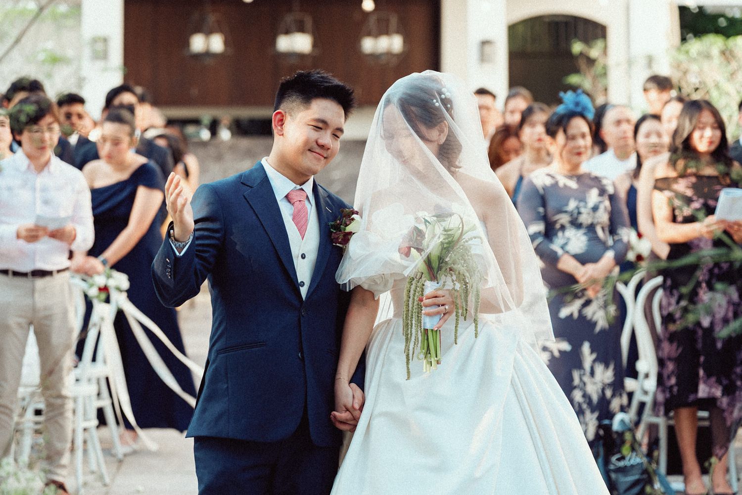A joyful wedding ceremony outdoors with guests watching as a couple walks down the aisle together.