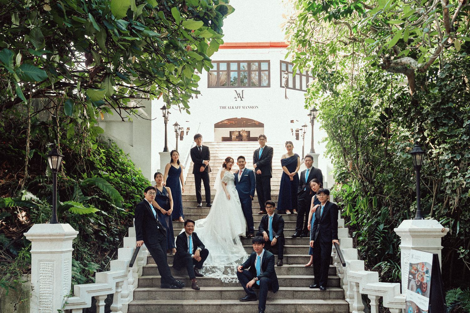 Wedding guests in formal attire gather on elegant white outdoor steps surrounded by lush greenery.