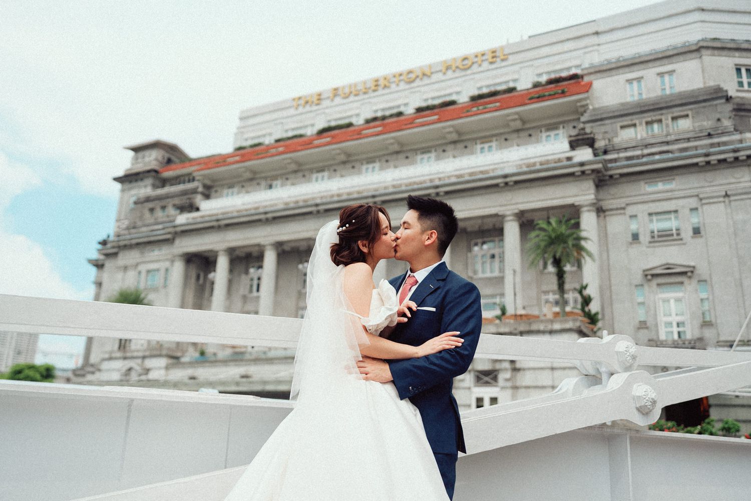 A couple shares a romantic kiss on the steps of a grand white stone building during their wedding photo session.