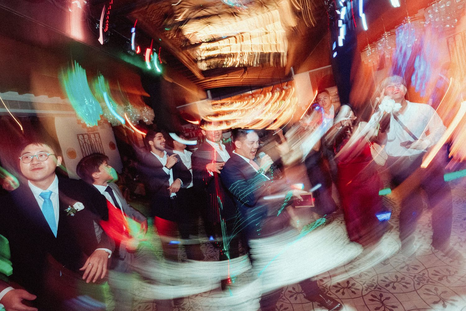 Motion-blurred dance floor scene at a wedding reception with dynamic lighting and swirling movements.