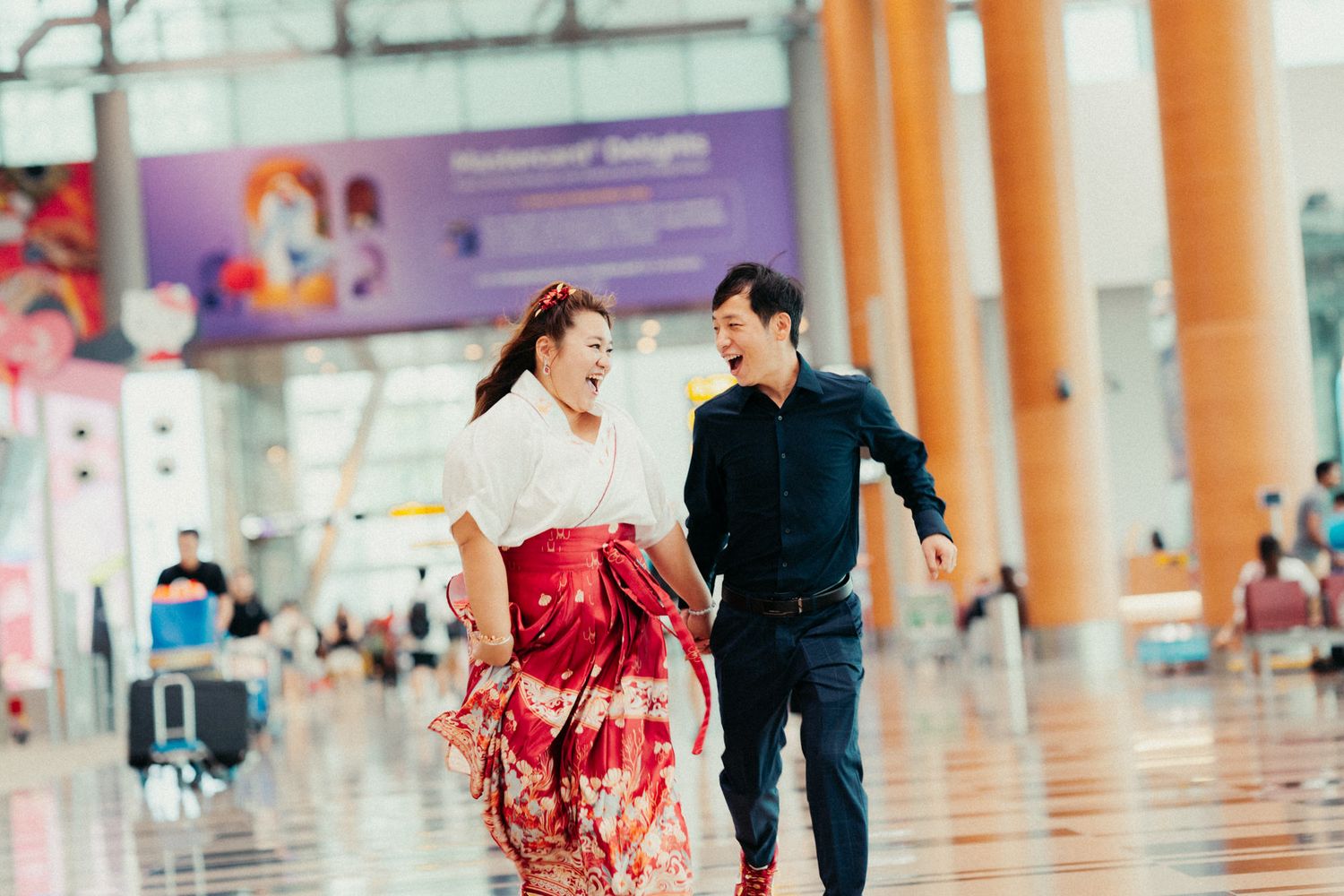 Joyful couple in traditional Japanese attire laughing and walking together inside a modern airport terminal.