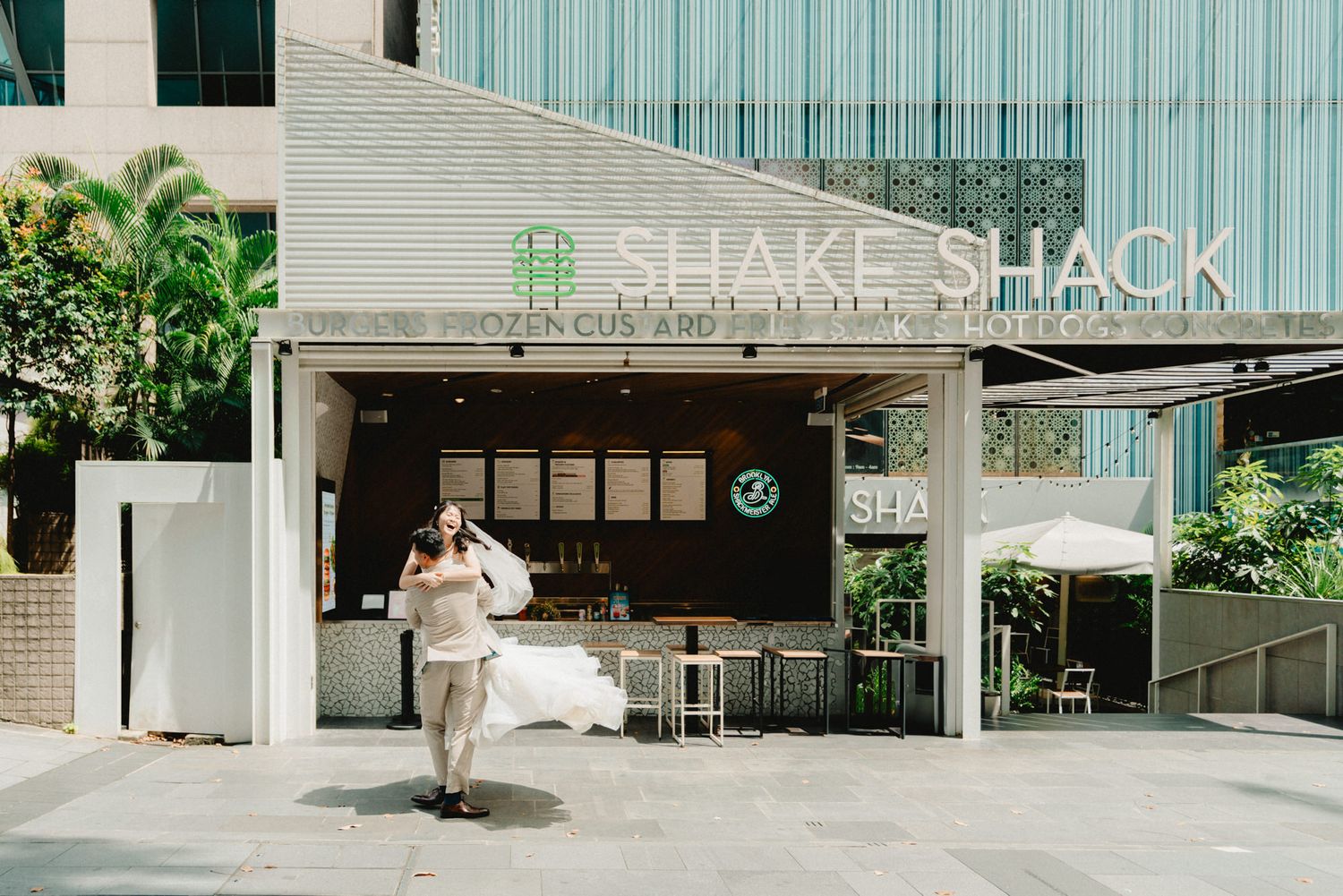 Shake Shack restaurant exterior with open facade, outdoor seating, and a woman walking by in an urban setting.