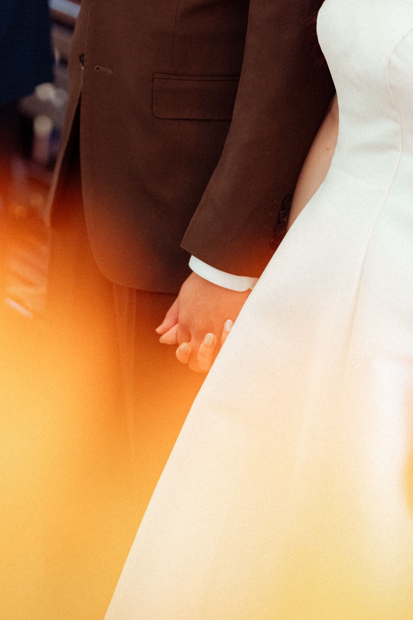 Bride and groom hold hands at the altar, wearing white gown and brown suit.