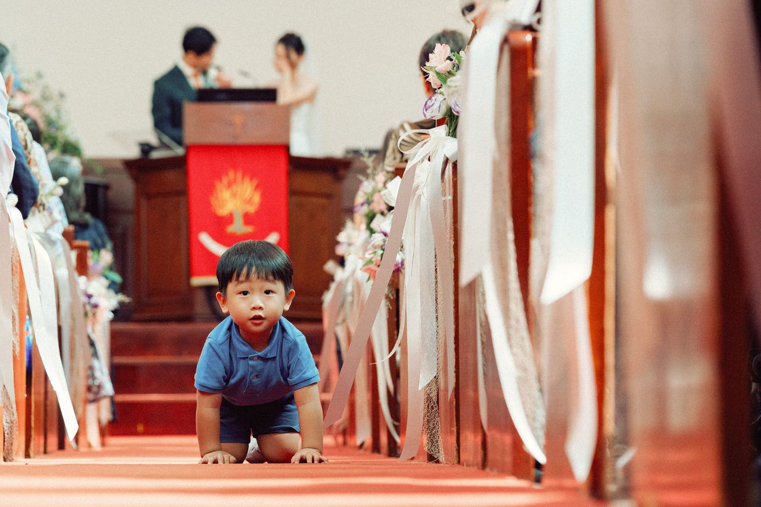 Church interior with red carpet aisle and white decorative elements during a wedding ceremony.