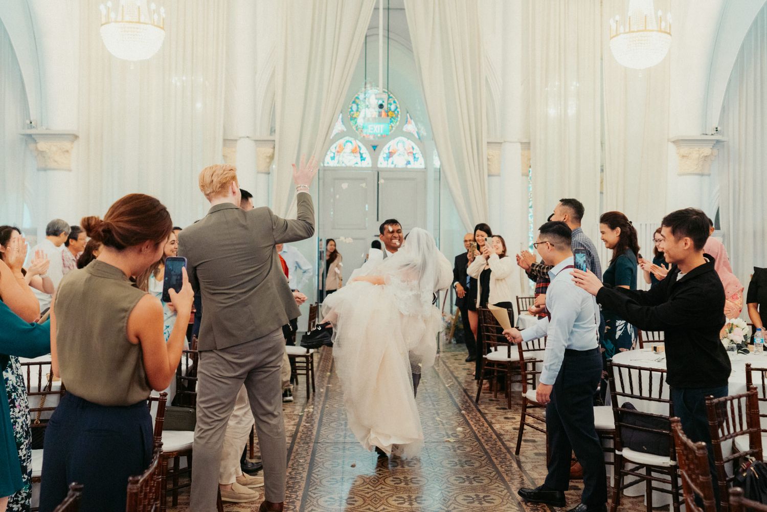 Joyful newlyweds walk down the aisle at elegant wedding venue as guests celebrate with applause.