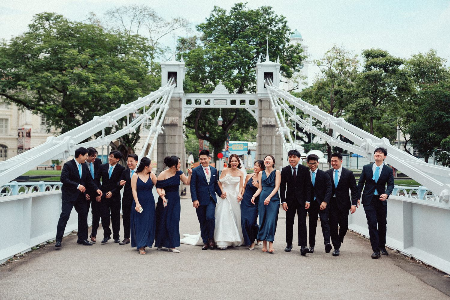 Wedding party poses together on a white ornate bridge in a scenic outdoor setting.