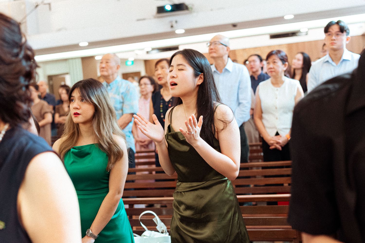 Women in elegant dresses stand in a church congregation during a wedding ceremony.