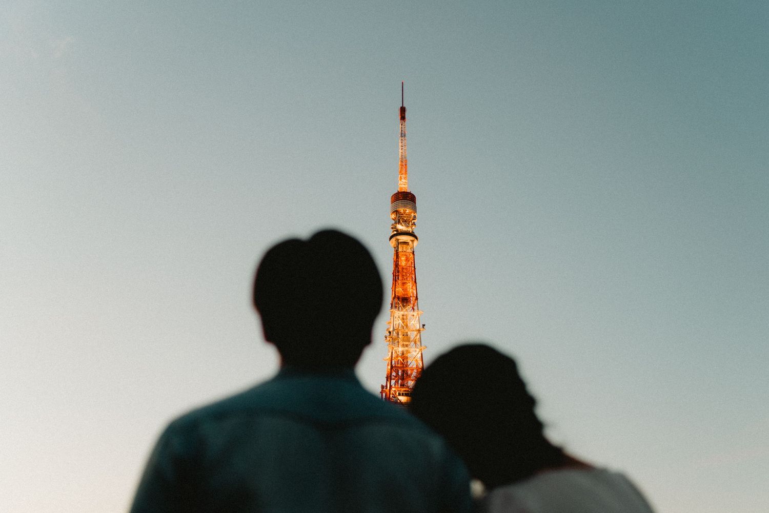 Silhouettes of people standing against a sunset sky with Tokyo Tower glowing orange in the background.