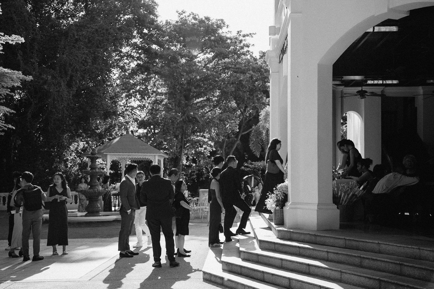 Black and white photograph of people gathering under architectural arches in an outdoor setting.
