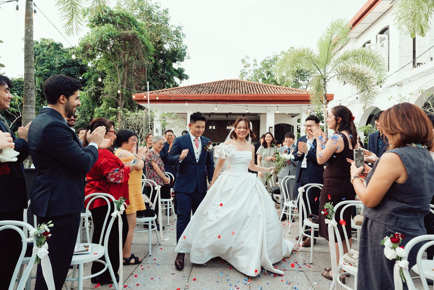 Newlyweds dance joyfully together during an outdoor wedding reception surrounded by guests on white chairs.