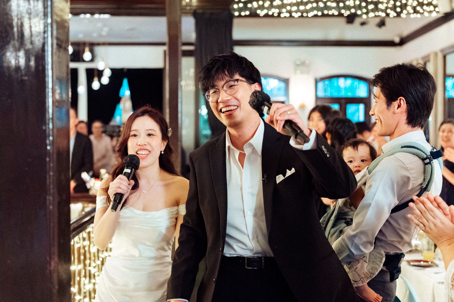 Bride and groom smiling and singing with microphones at elegant wedding reception.
