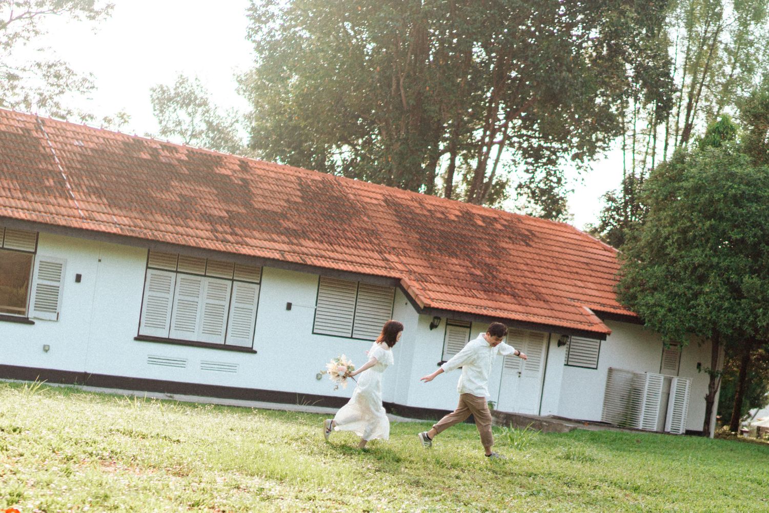 A row of small white rural buildings with red tile roofs nestled among trees on a sunny day.