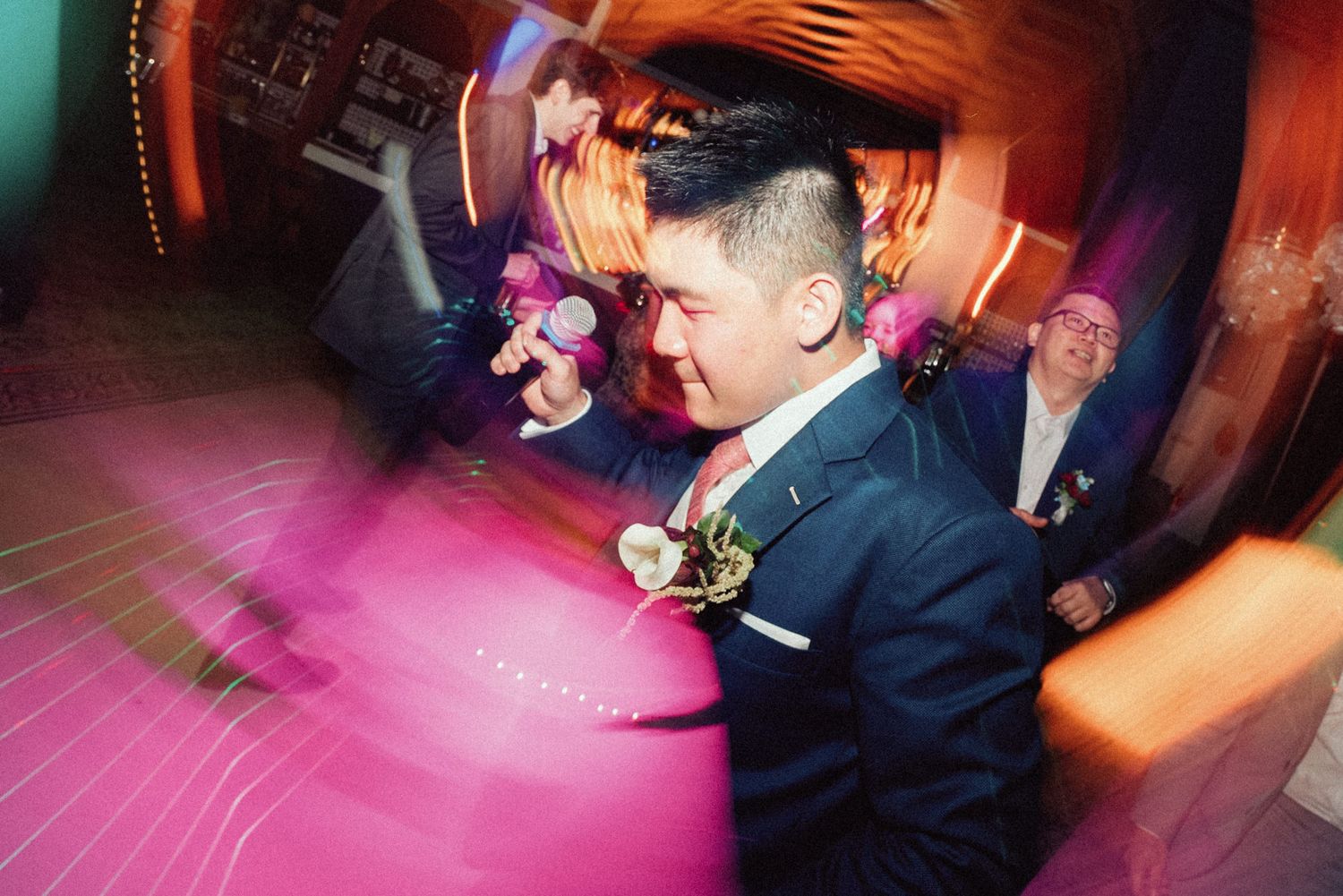 A couple dancing together at a wedding reception with pink and purple lighting on the dance floor.