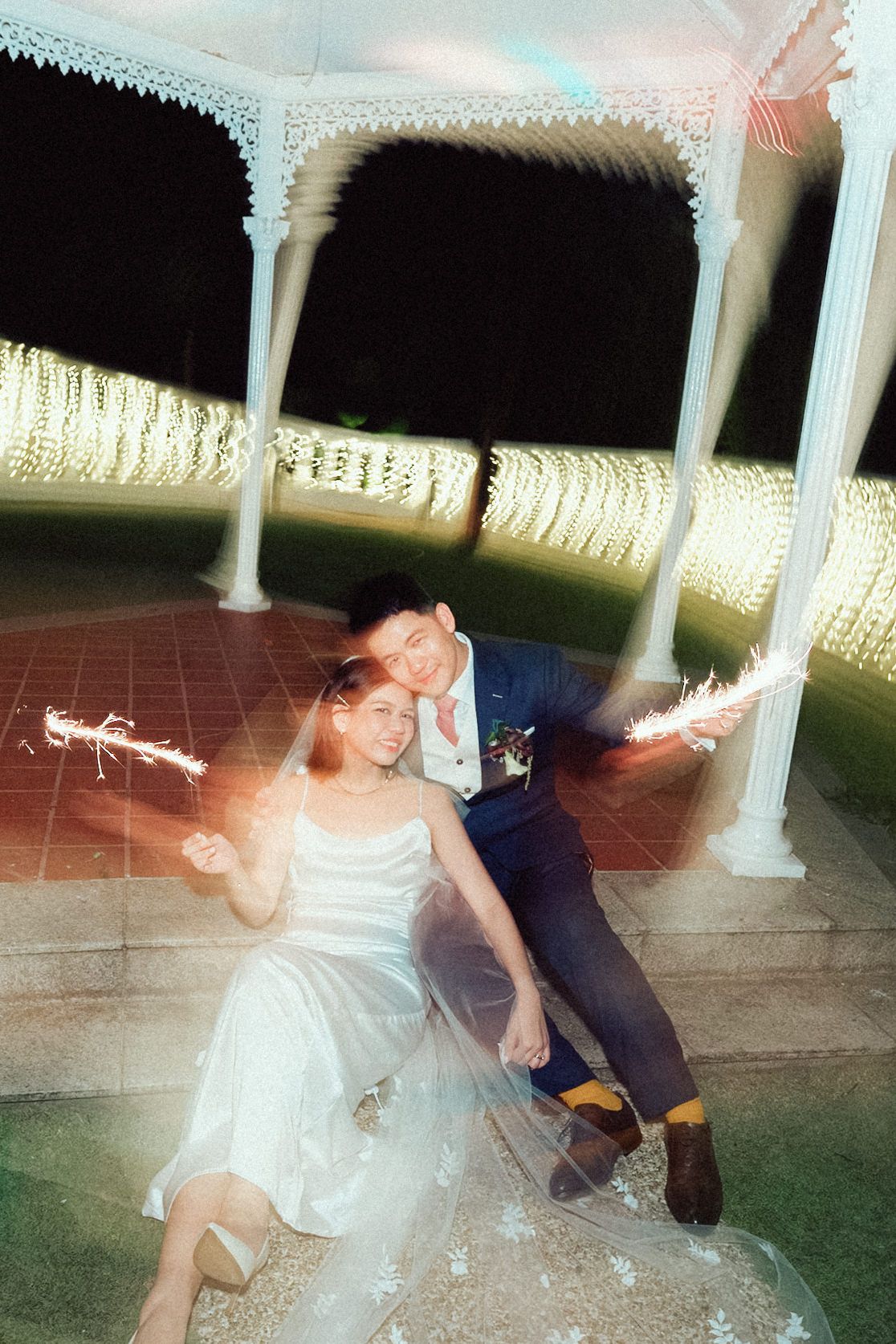 A couple dances together at an outdoor gazebo venue with sparklers creating light trails in the evening.