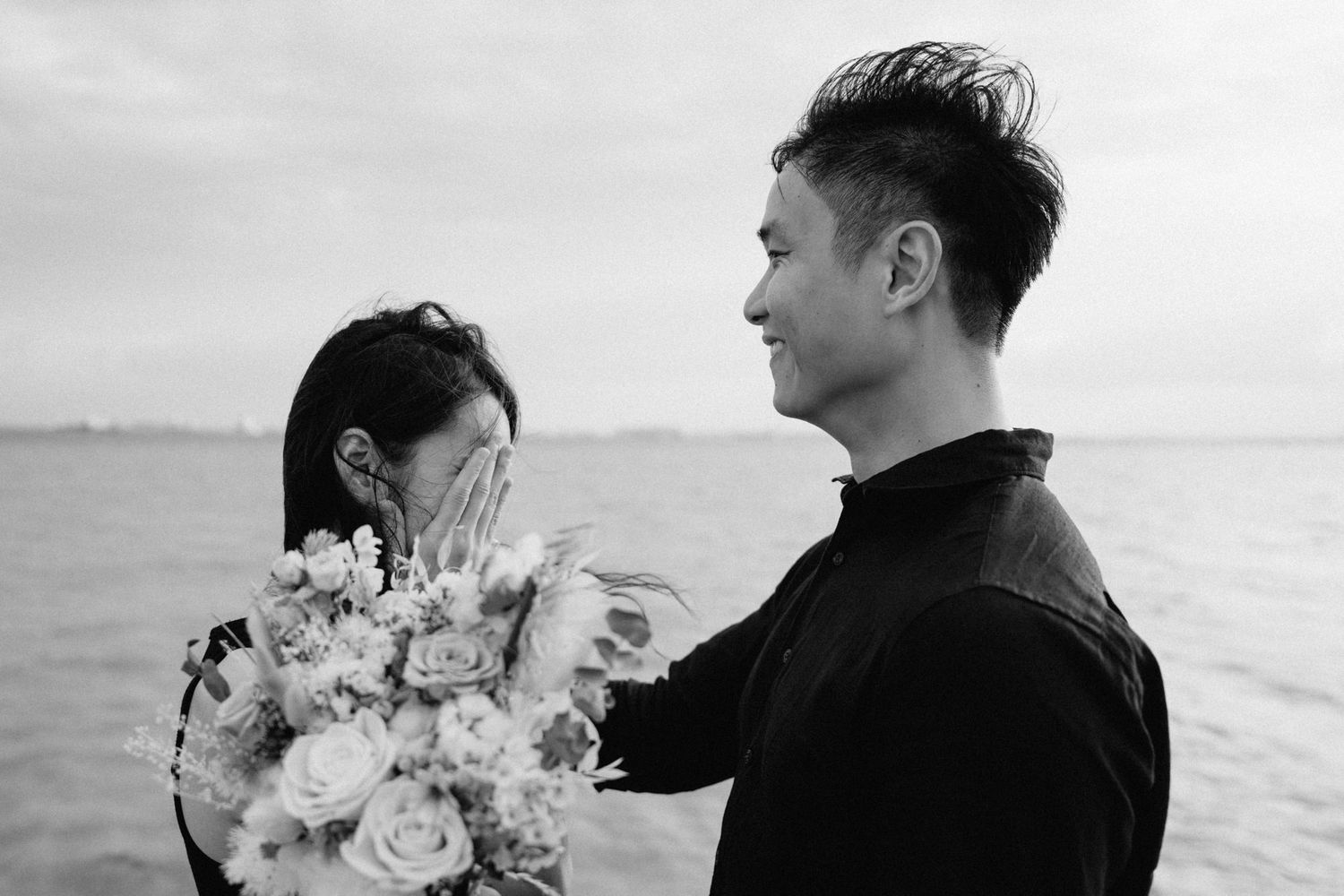 A couple embraces on a rocky beach during a romantic photoshoot.