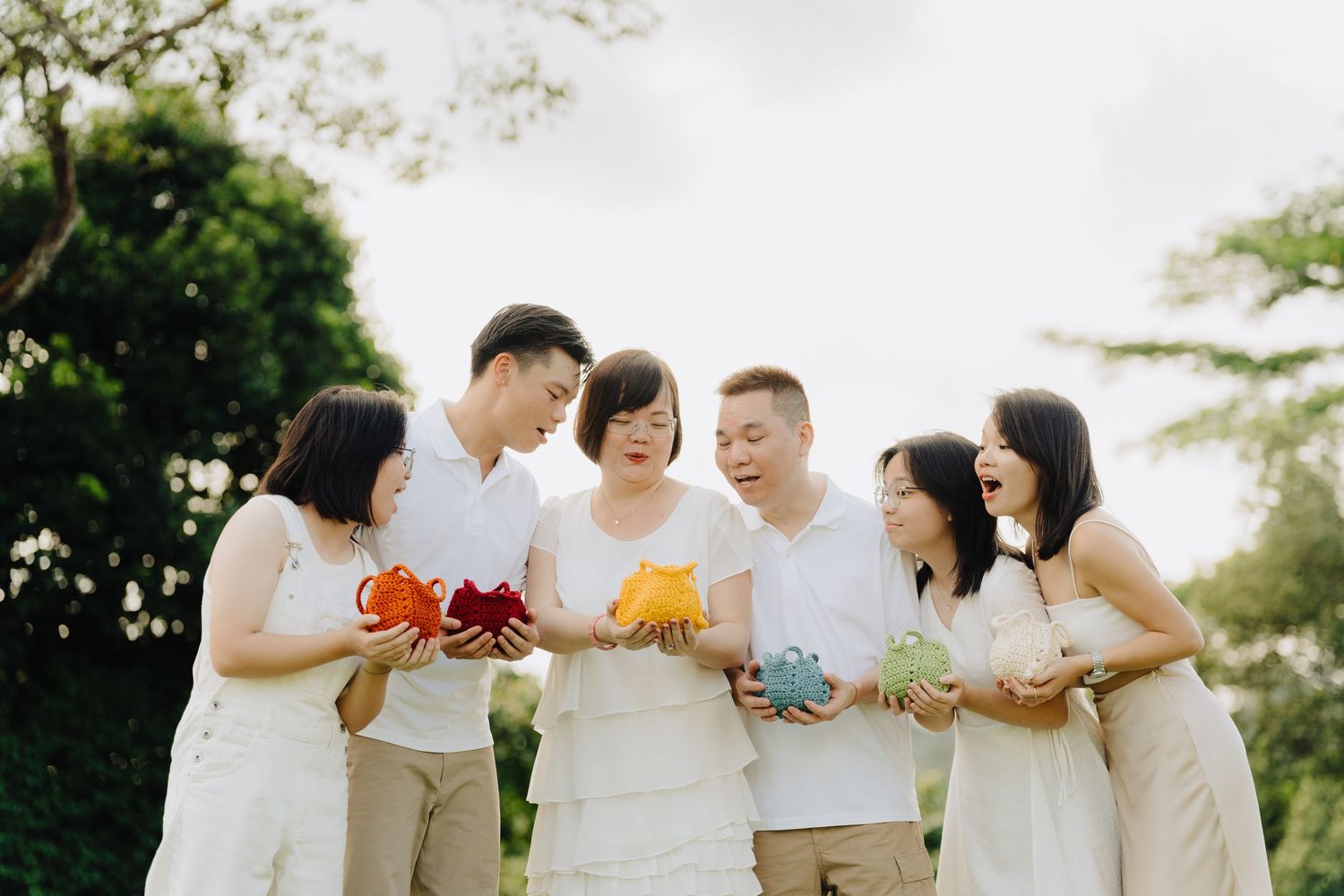 A group in white and beige outfits stands in a line outdoors while holding colorful decorative items.