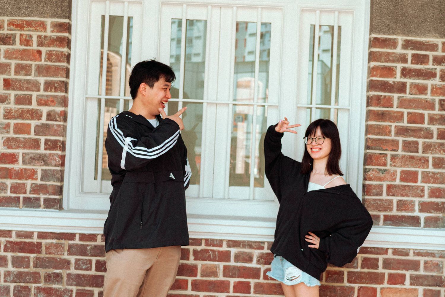 Students in black jackets gather in front of a brick building exterior during a casual social interaction.