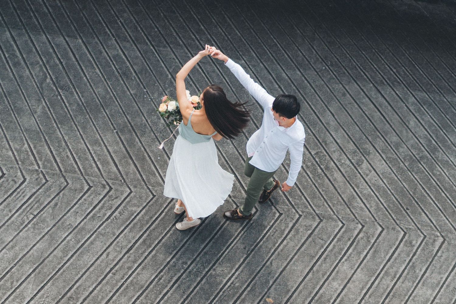 A couple in wedding attire walks along a patterned stone pathway while holding hands.