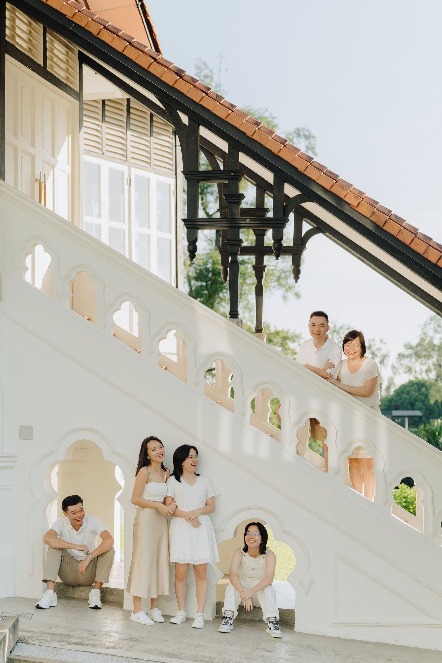 Family wearing white and beige outfits poses together on white architectural steps in a progressive series of photos.